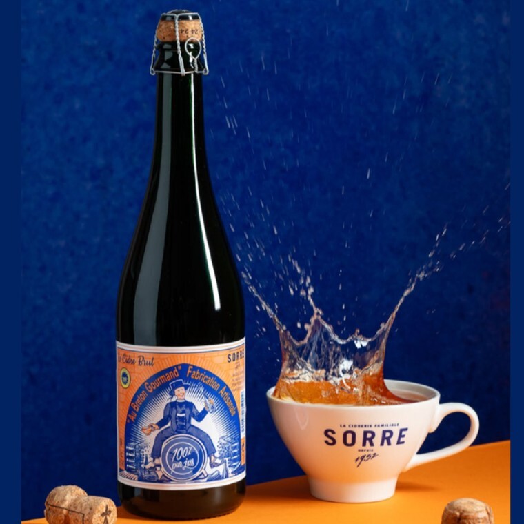 Bottle of Au Breton Gourmand Brut French dry cider from Brittany, splashing into a traditional Sorre cider bowl