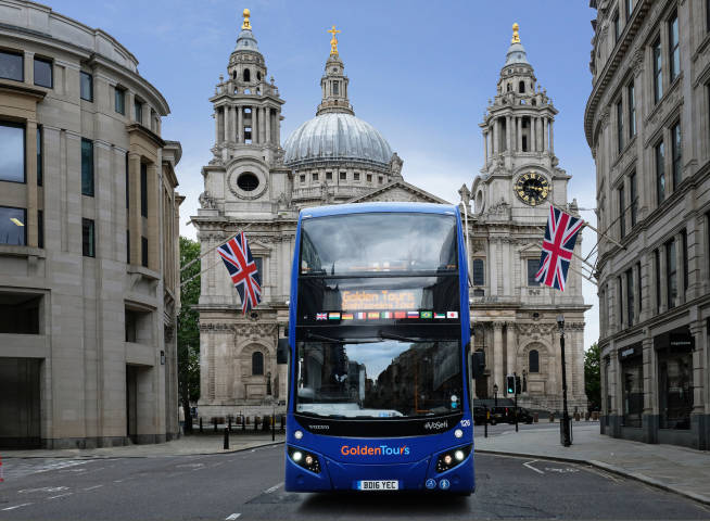 Golden Tours bus driving down a road with large buildings and union jack flags