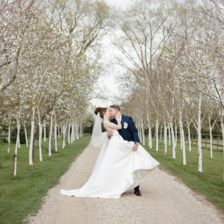 Bride and groom sharing a romantic dip kiss on their wedding day, surrounded by natural light and blossoming atmosphere.