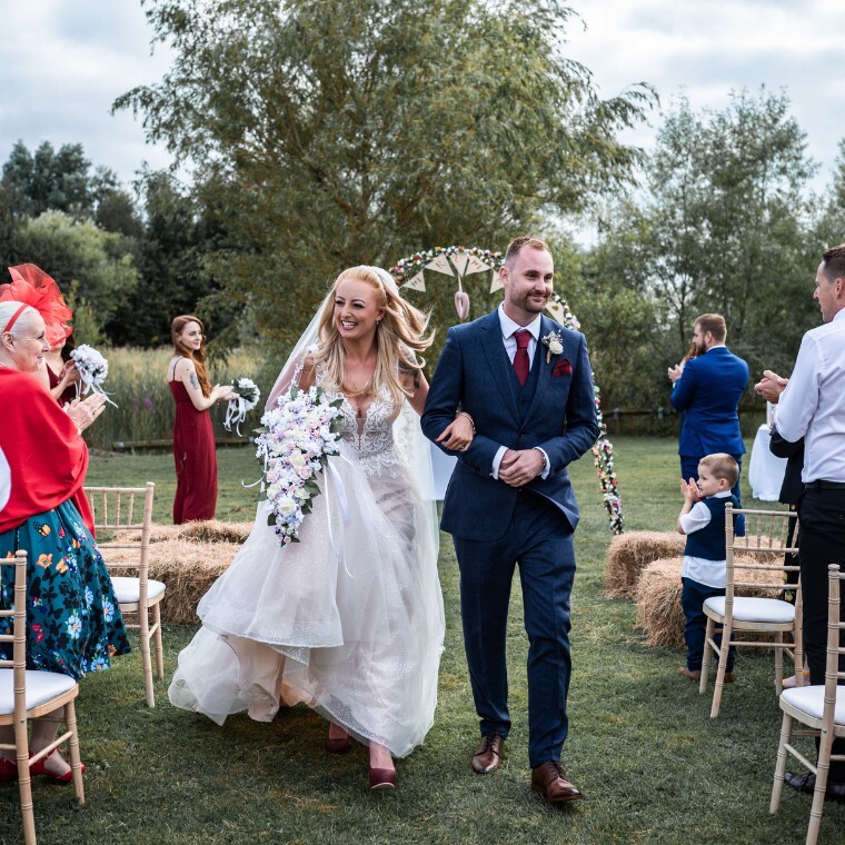 Loving couple just wed, walking down the isle of our outdoor space, Willow Corner at the Millennium Country Park
