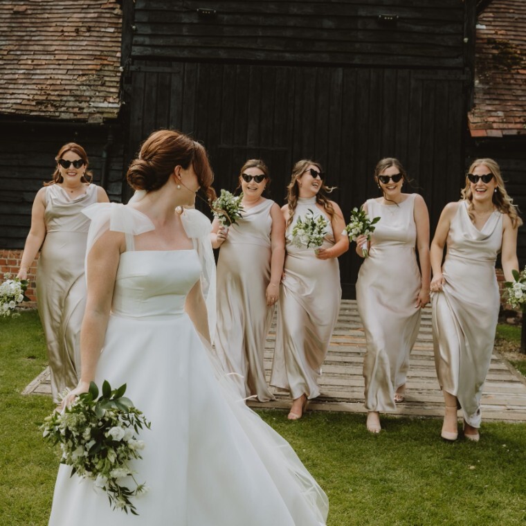 Bride walking with her bridesmaids in champagne dresses outside a rustic barn venue in Oxfordshire, photographed by V & H Photography