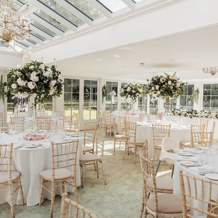 Bright and elegant Orangery at Hayne House in Kent, featuring open French doors, manicured gardens, and vibrant floral arrangements, perfect for a picturesque wedding celebration. 