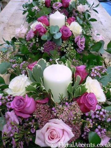 Table centre designs with assorted flowers & foliage and a pillar candle - by Floral Accents.