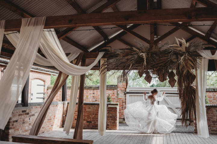 Barn courtyard area with neutral coloured drapes hanging from the beams and a bride in the corner twirling her dress