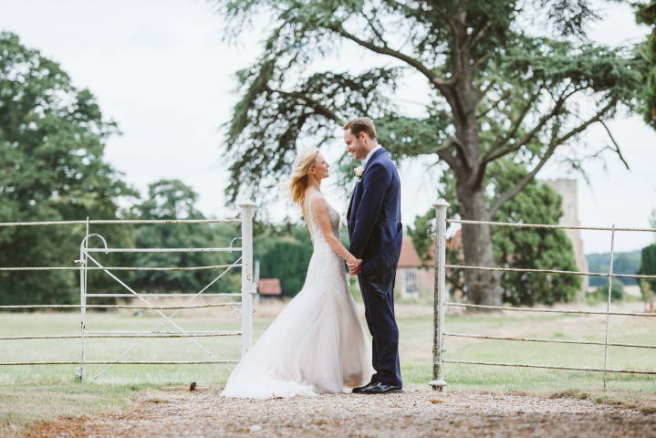Bride and Groom on wedding day at Gosfield hall, stand with white fence, tree behind