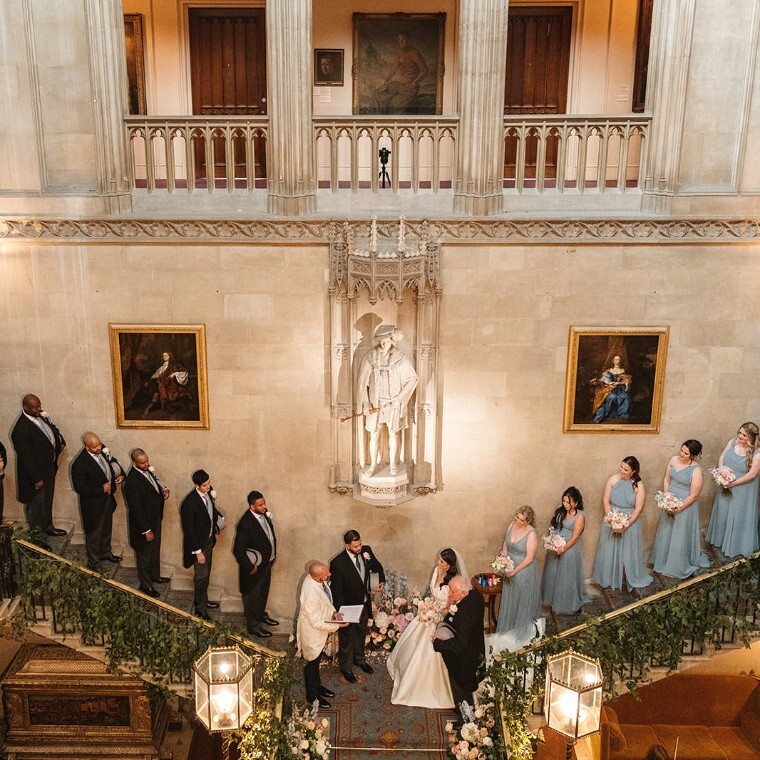 Luxury wedding ceremony at Ashridge House, with bride and groom exchanging vows on a grand staircase surrounded by their bridal party