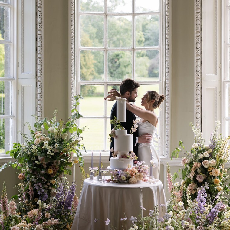 A bride and groom embrace surrounded by flowers inside a historic house