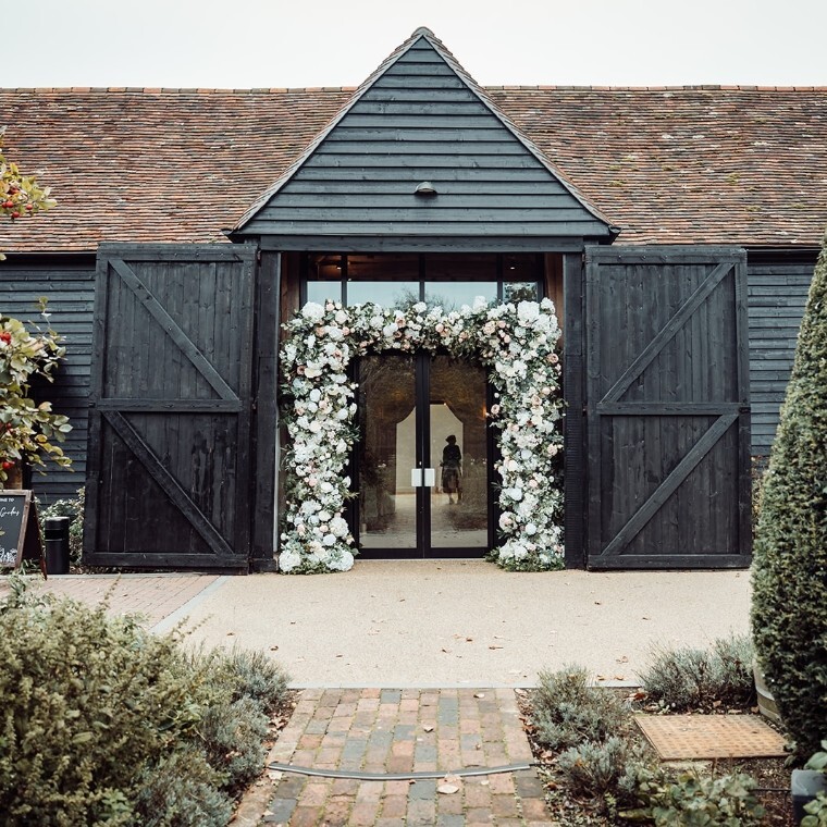 Exterior of Alfriston Gardens barn with floral archway at entrance