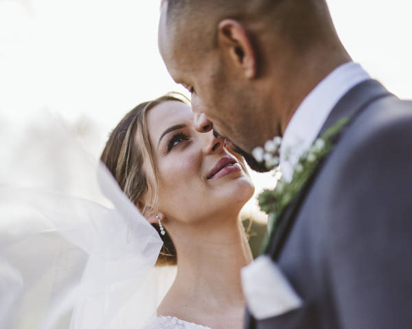 Bride has close embrace with groom, wedding veil floats towards camera