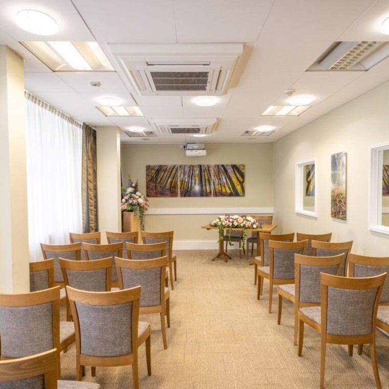 The George Room ceremony space in CHeltenham register office. Grey and oak chairs, images of Cheltenham and pink and white silk flower display