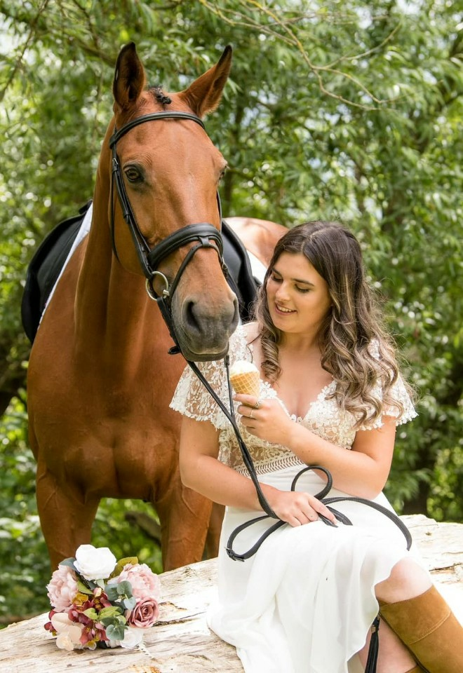 bride sat on fallen tree feeding a horse an ice cream at her wedding